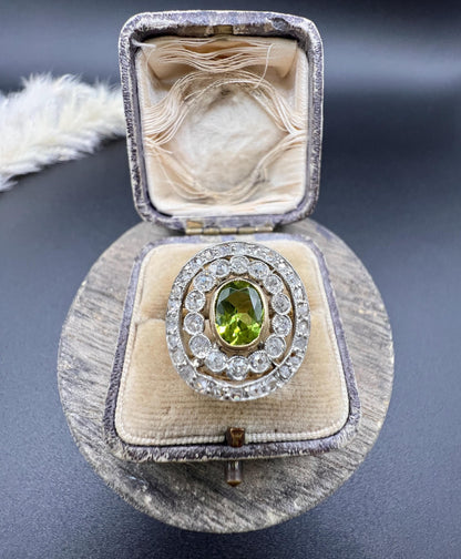 An oval peridot and old cut diamond fancy cluster ring in yellow gold and platinum, in a ring box