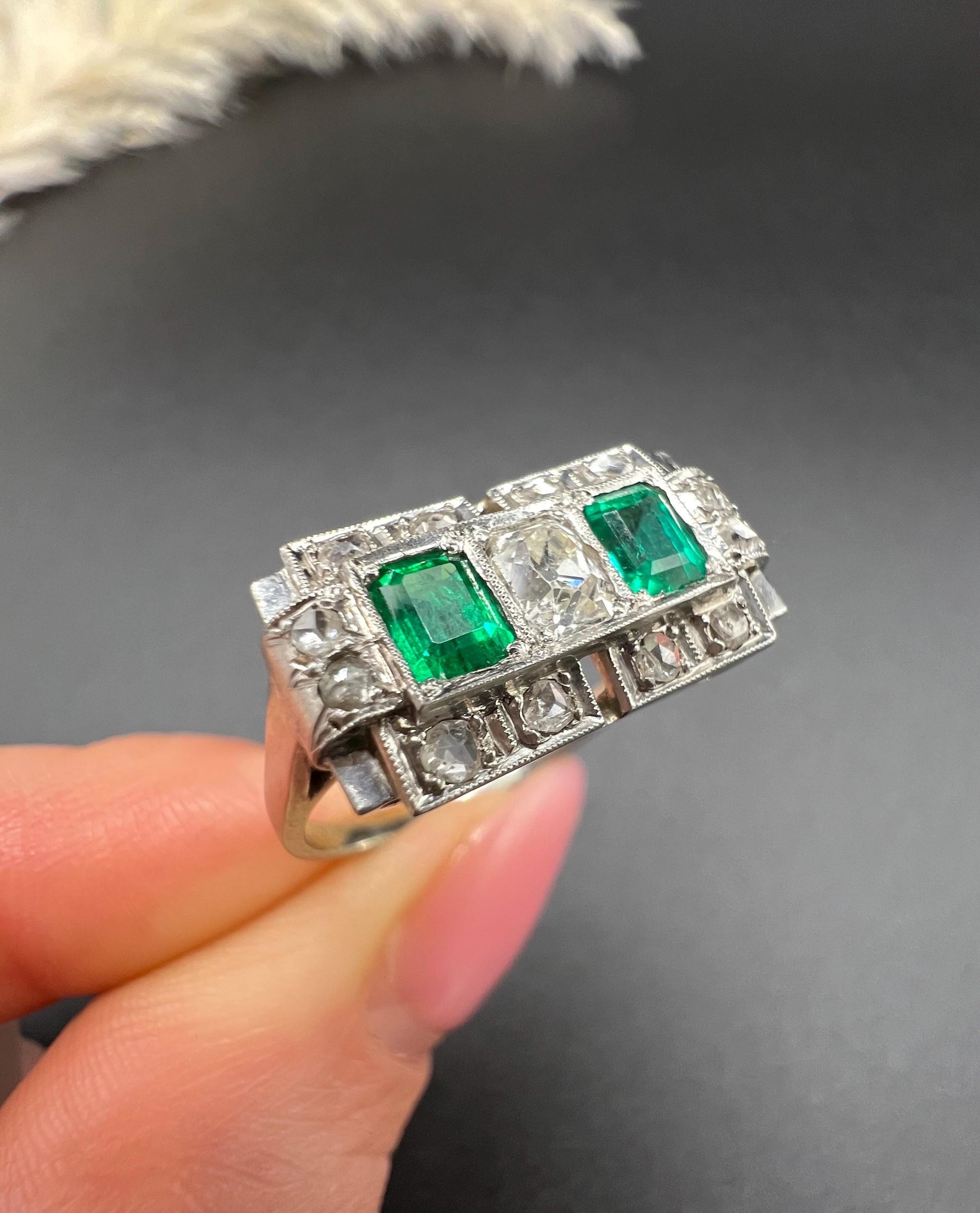 An emerald and old cut diamond rectangular ring in platinum, held in a hand