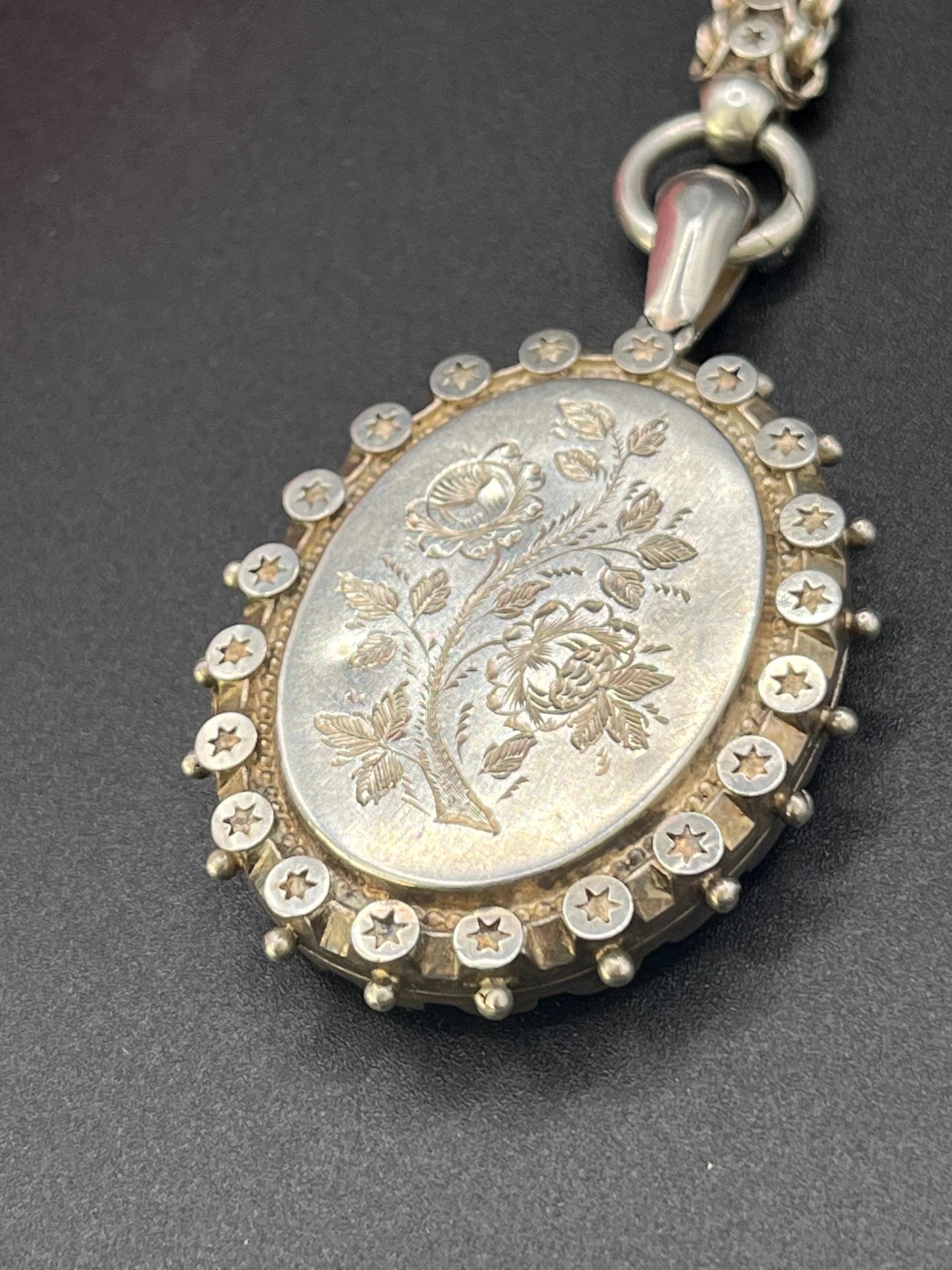 A silver oval locket with floral engraving on a silver book chain collar
