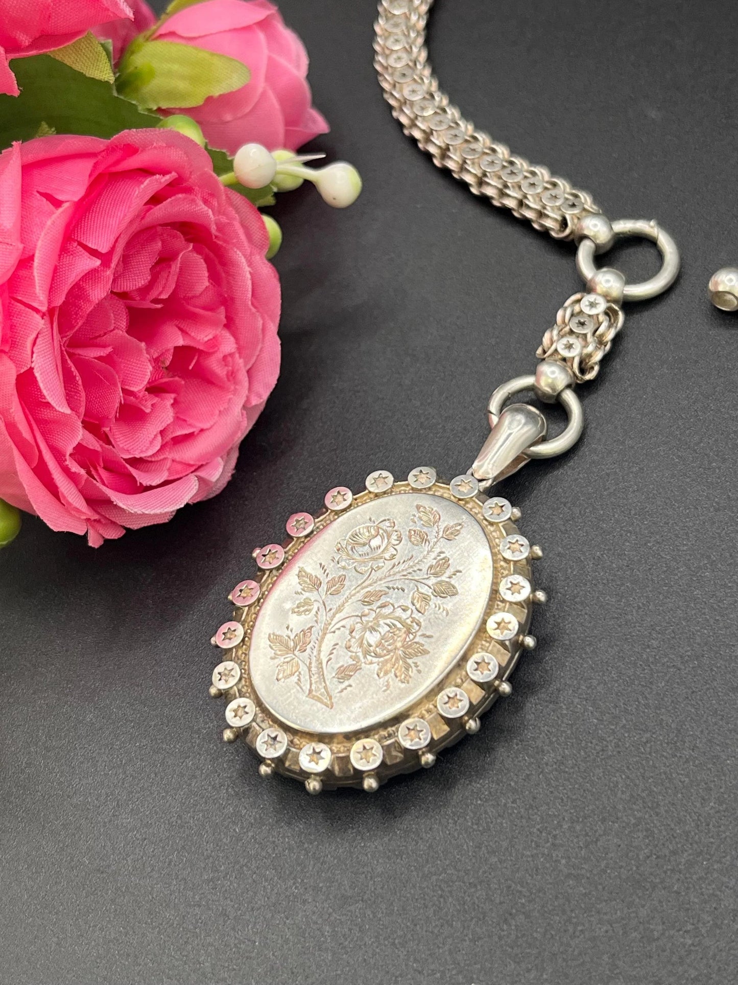 A silver oval locket with floral engraving on a silver book chain collar