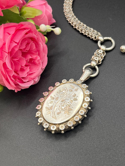 A silver oval locket with floral engraving on a silver book chain collar
