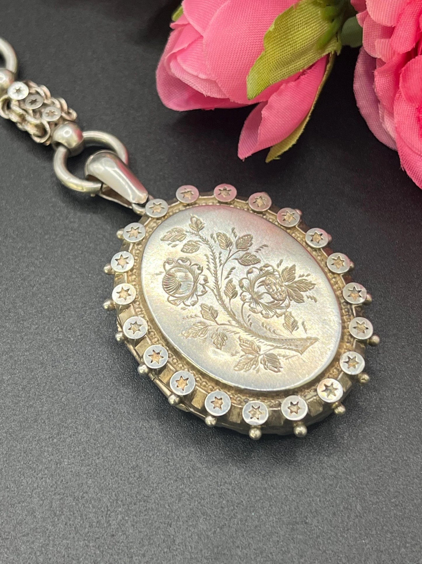 A silver oval locket with floral engraving on a silver book chain collar
