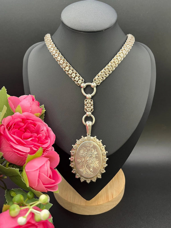 A silver oval locket with floral engraving on a silver book chain collar