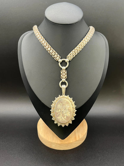 A silver oval locket with floral engraving on a silver book chain collar