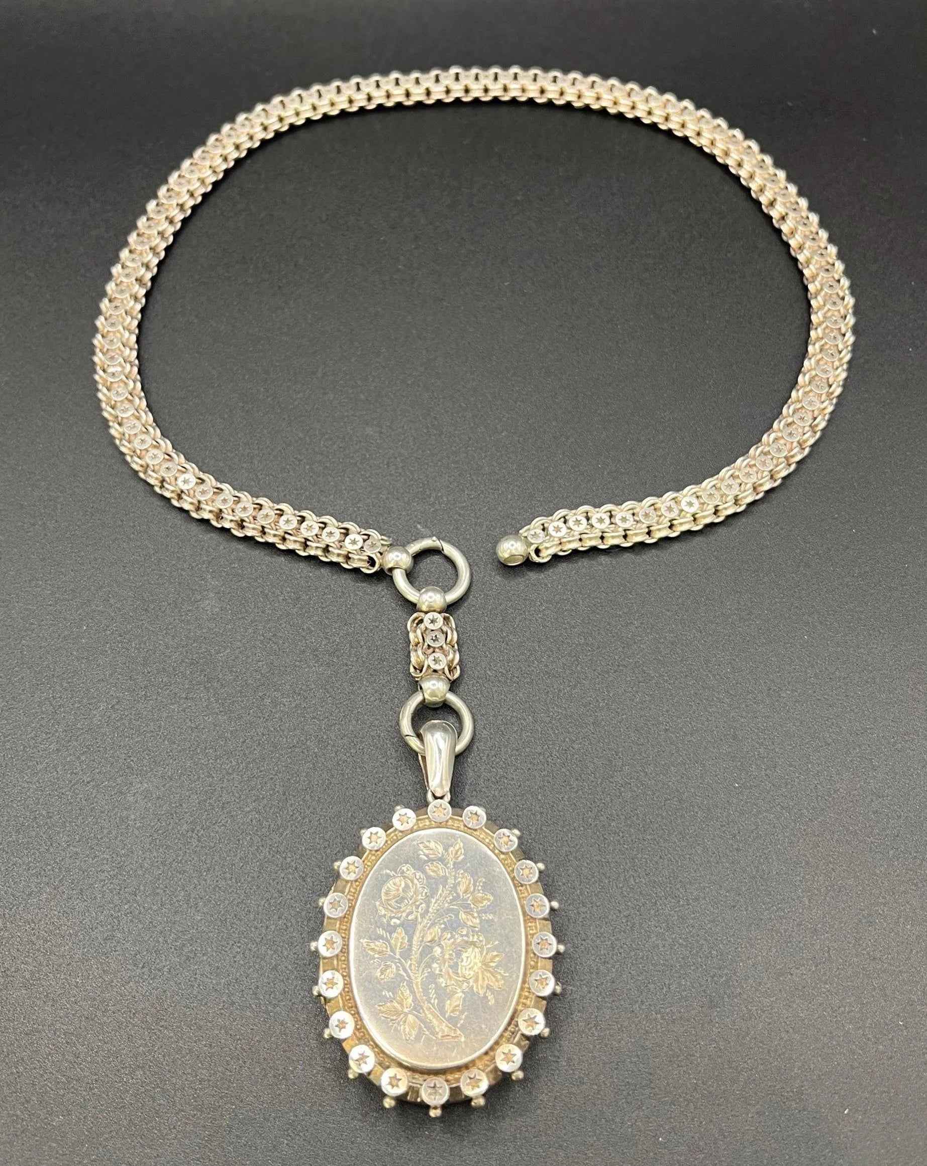 A silver oval locket with floral engraving on a silver book chain collar