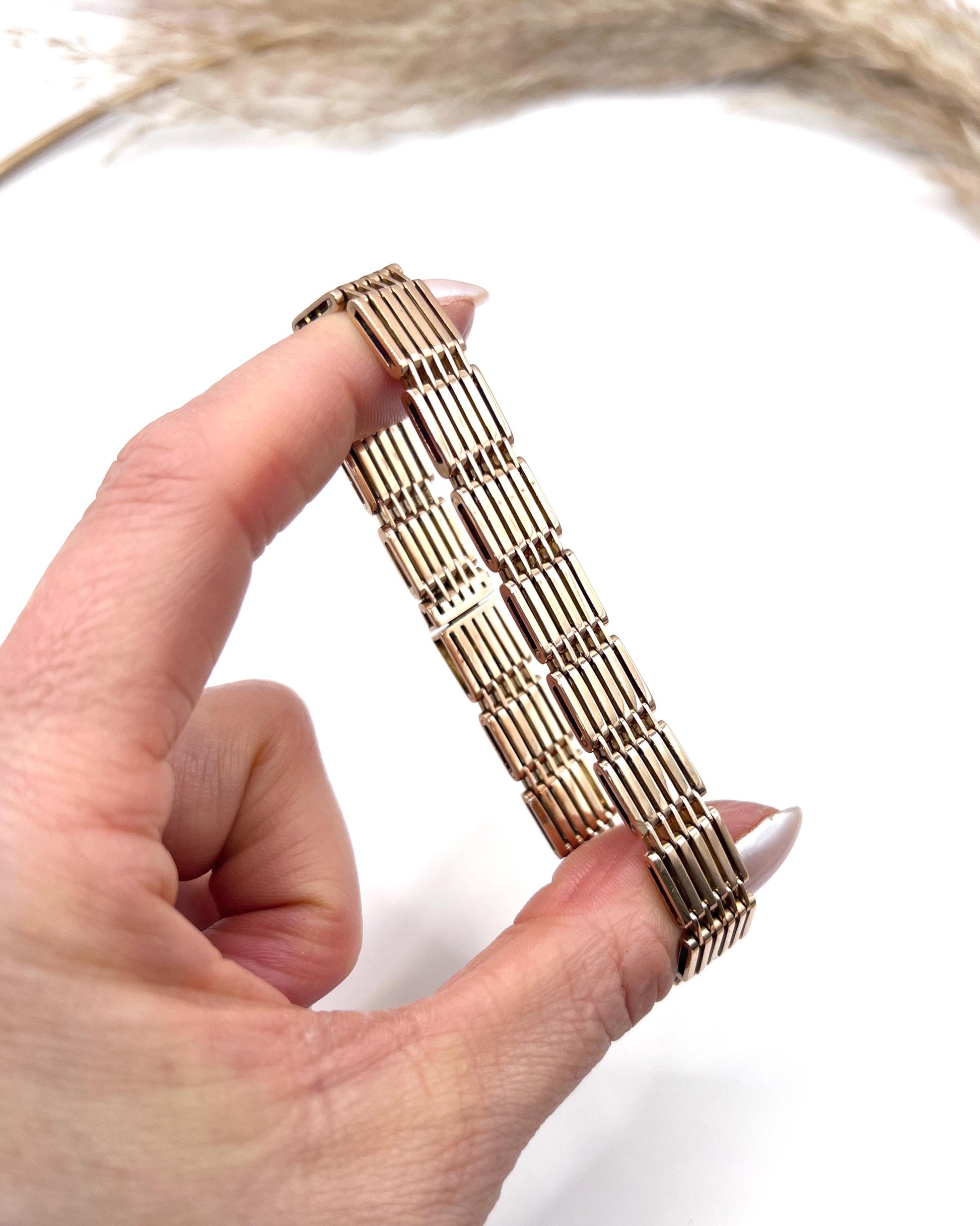 A yellow-rose gold gate style bracelet, held in a hand