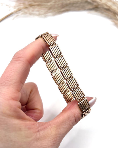 A yellow-rose gold gate style bracelet, held in a hand