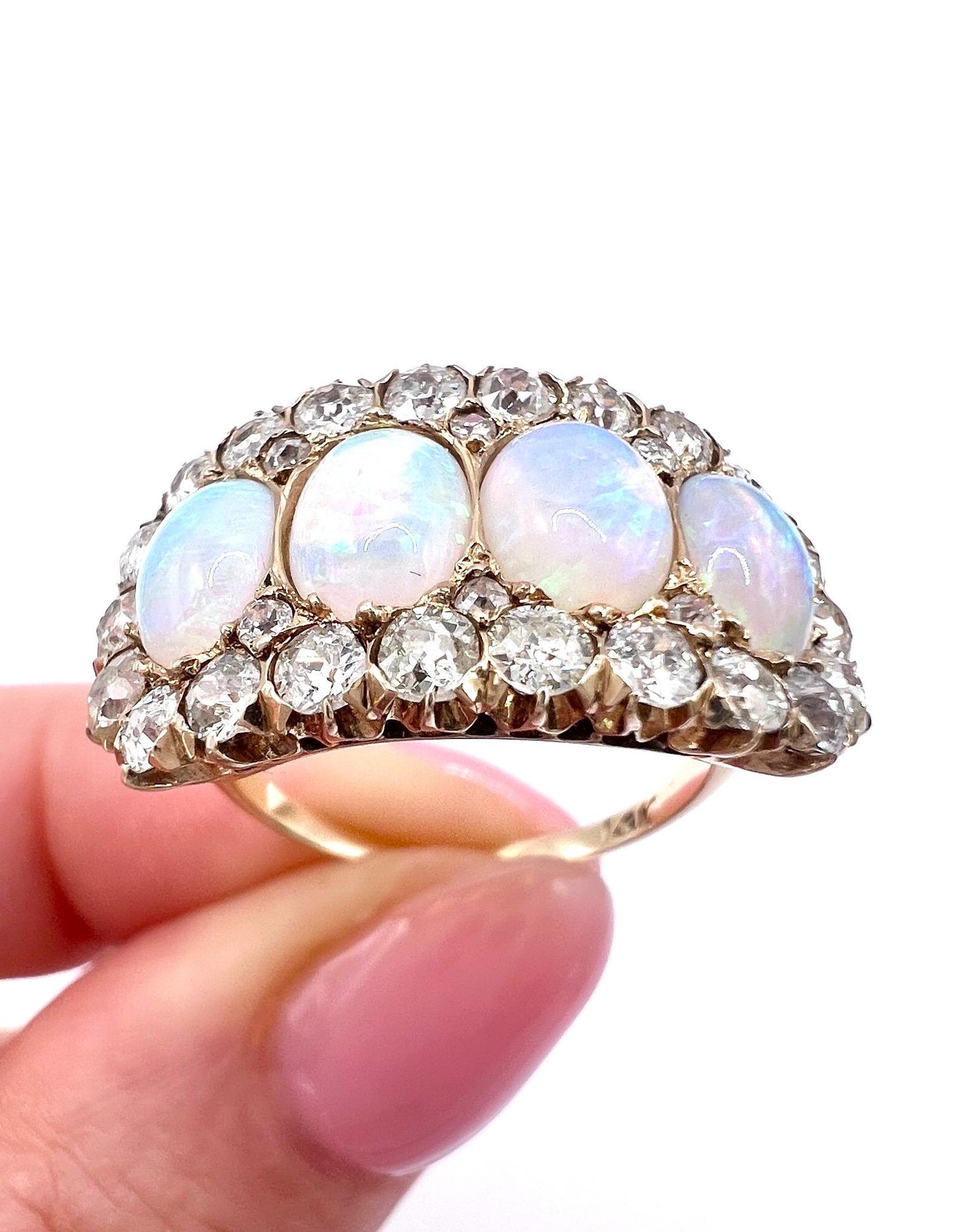 An antique oval opal and old cut diamond cluster row ring in yellow gold, held in a hand