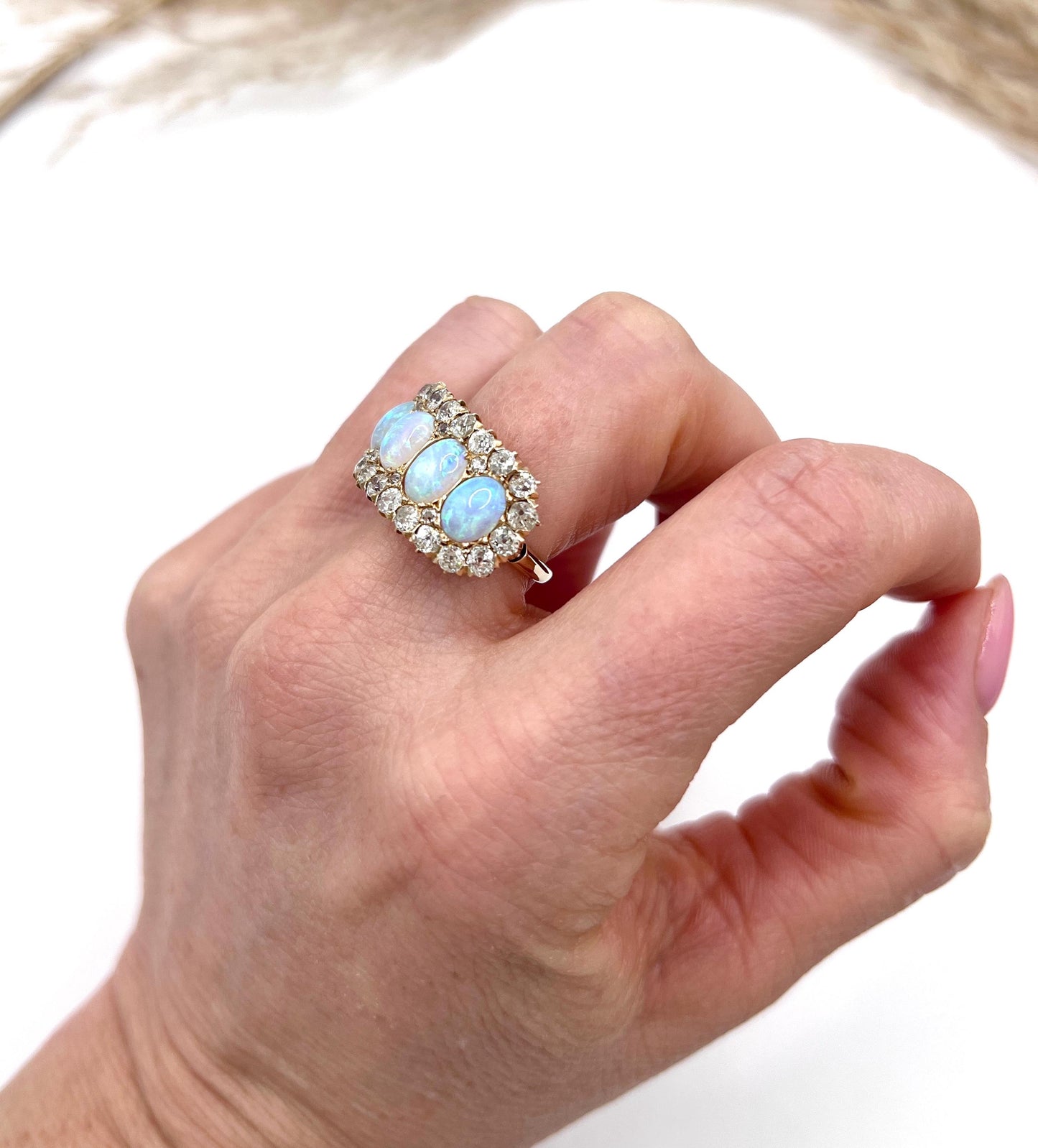 An antique oval opal and old cut diamond cluster row ring in yellow gold, modelled on a hand