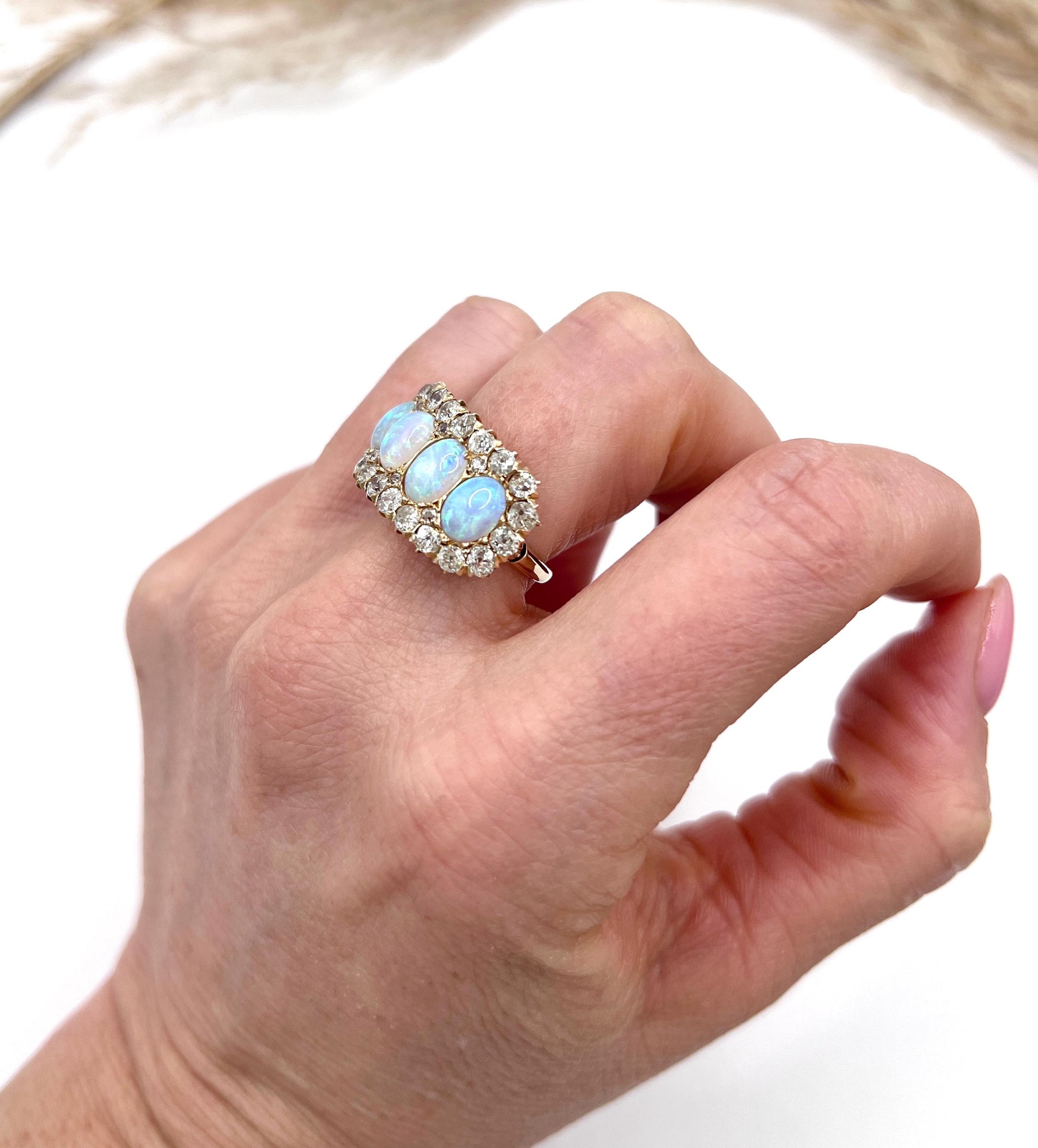 An antique oval opal and old cut diamond cluster row ring in yellow gold, modelled on a hand