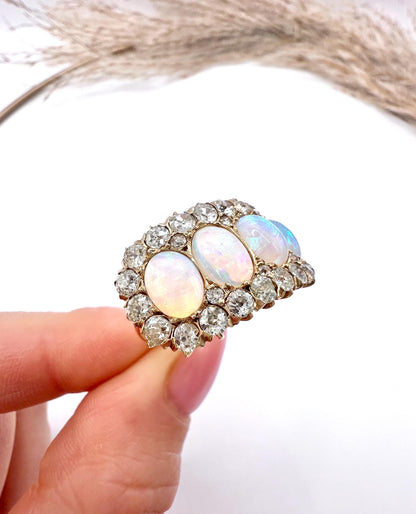 An antique oval opal and old cut diamond cluster row ring in yellow gold, held in a hand