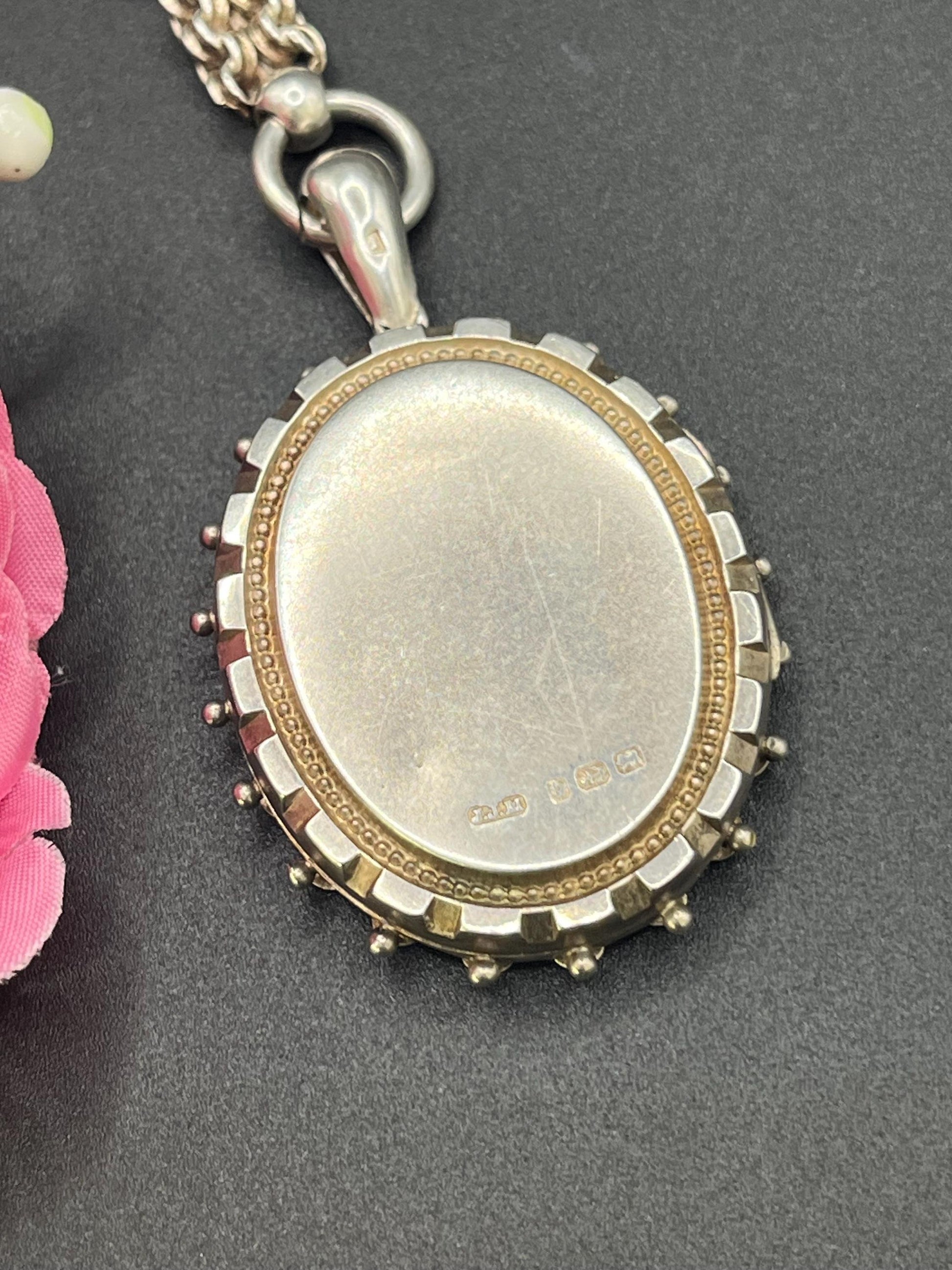 A silver oval locket with floral engraving on a silver book chain collar