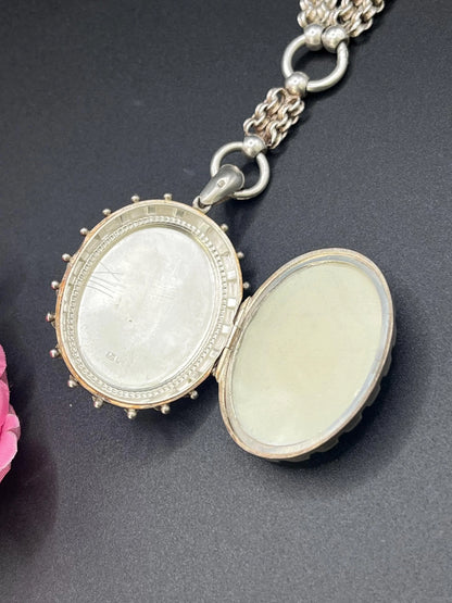 A silver oval locket with floral engraving on a silver book chain collar