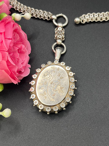 A silver oval locket with floral engraving on a silver book chain collar