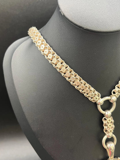 A silver oval locket with floral engraving on a silver book chain collar