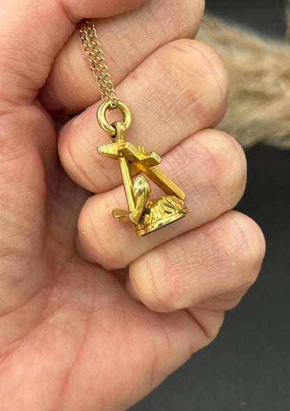 A yellow gold faith, hope and charity fob, with a heart-shaped bloodstone base, with a chain, held in a hand