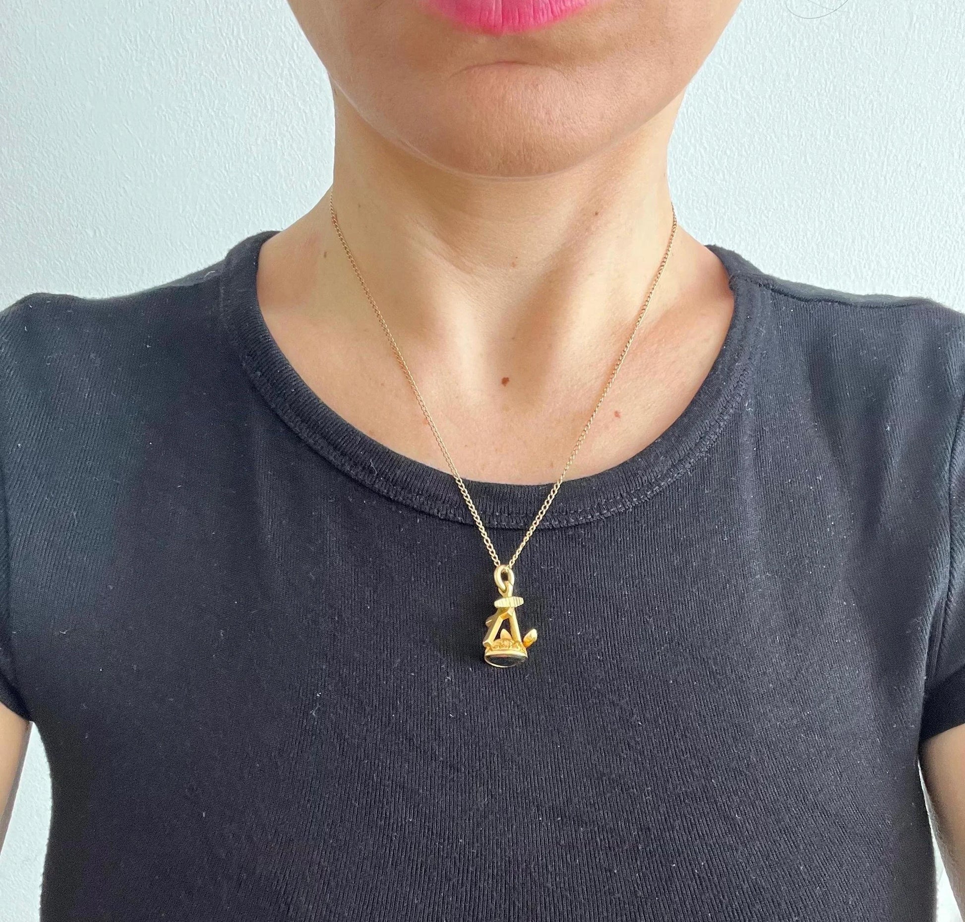 A yellow gold faith, hope and charity fob, with a heart-shaped bloodstone base, with a chain, modelled by a woman wearing a black top