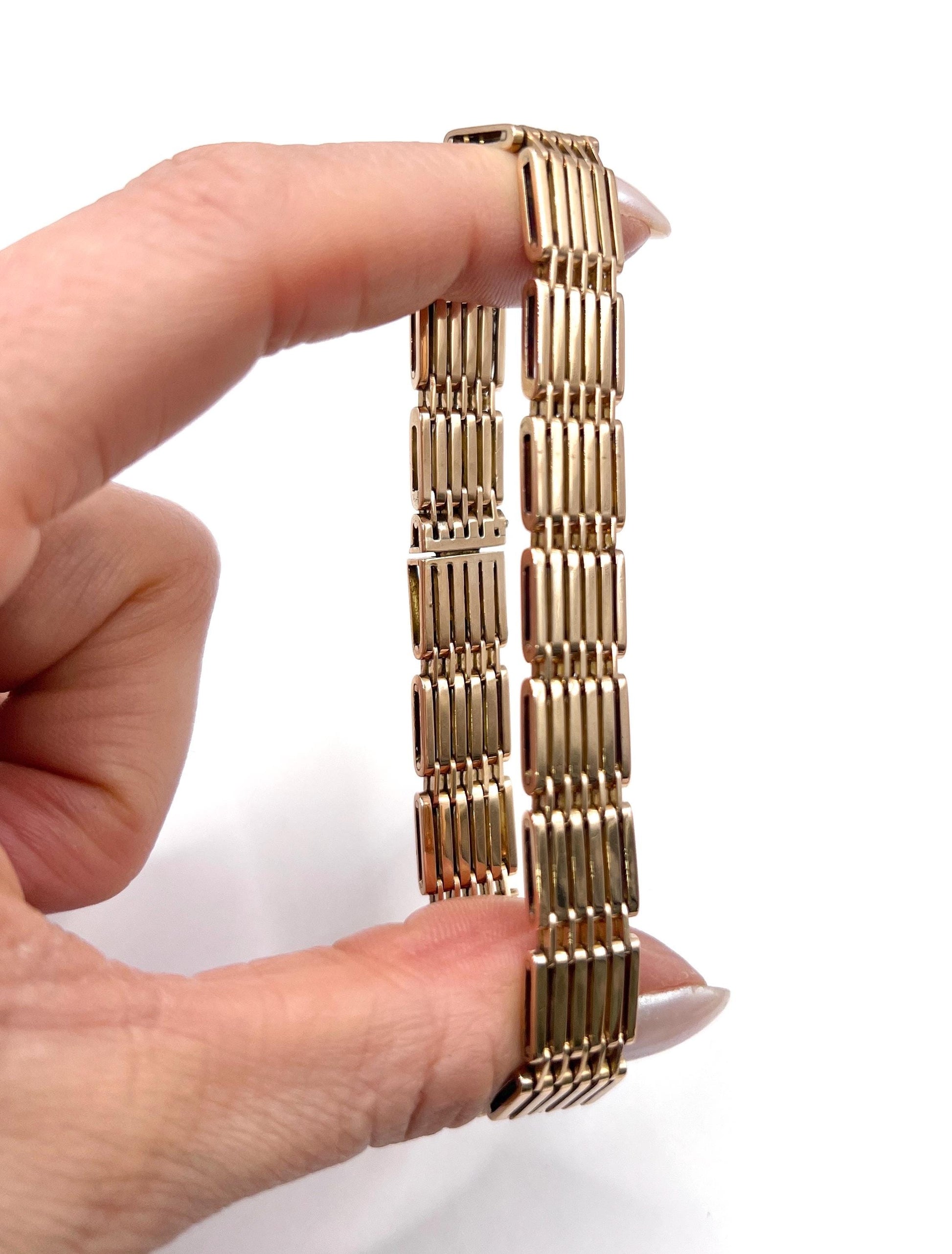 A yellow-rose gold gate style bracelet, held in a hand