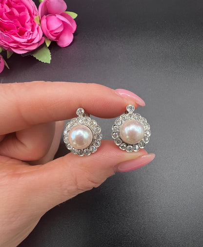 A pair of pearl and old cut diamond floral cluster earrings, held in a hand