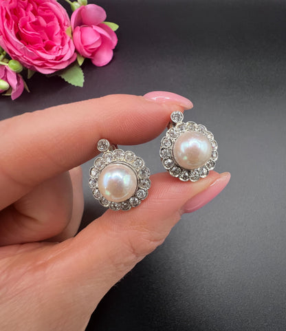 A pair of pearl and old cut diamond floral cluster earrings, held in a hand