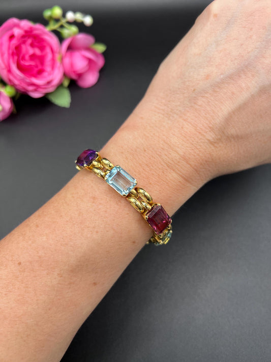An emerald cut multi-gemstone bracelet in yellow gold, modelled on a wrist