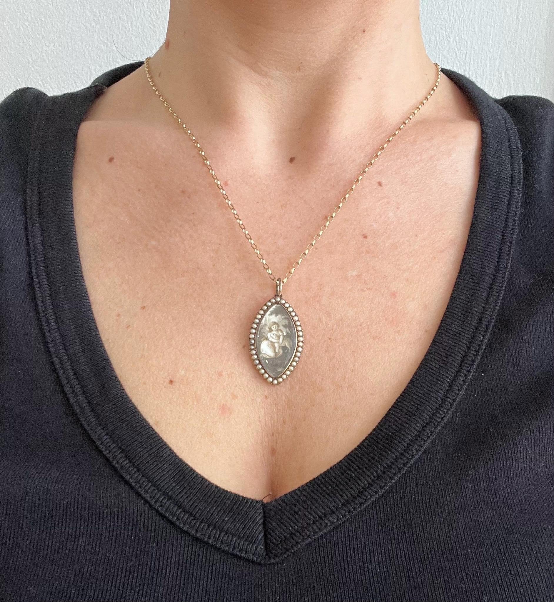 A navette shaped yellow gold seed pearl pendant with a miniature portrait, with a chain, modelled by a woman wearing a black top