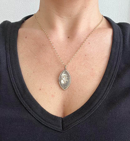 A navette shaped yellow gold seed pearl pendant with a miniature portrait, with a chain, modelled by a woman wearing a black top