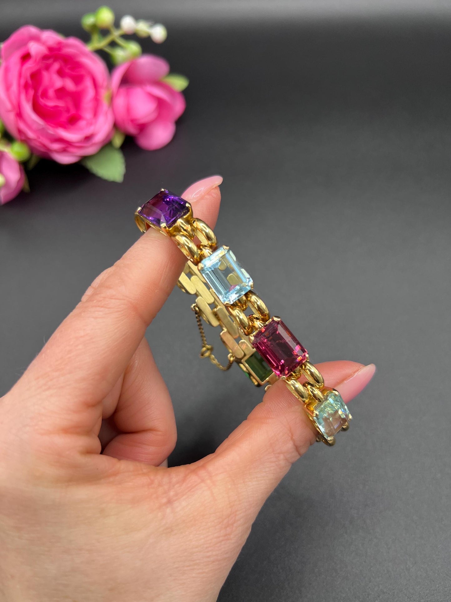 An emerald cut multi-gemstone bracelet in yellow gold, held in a hand