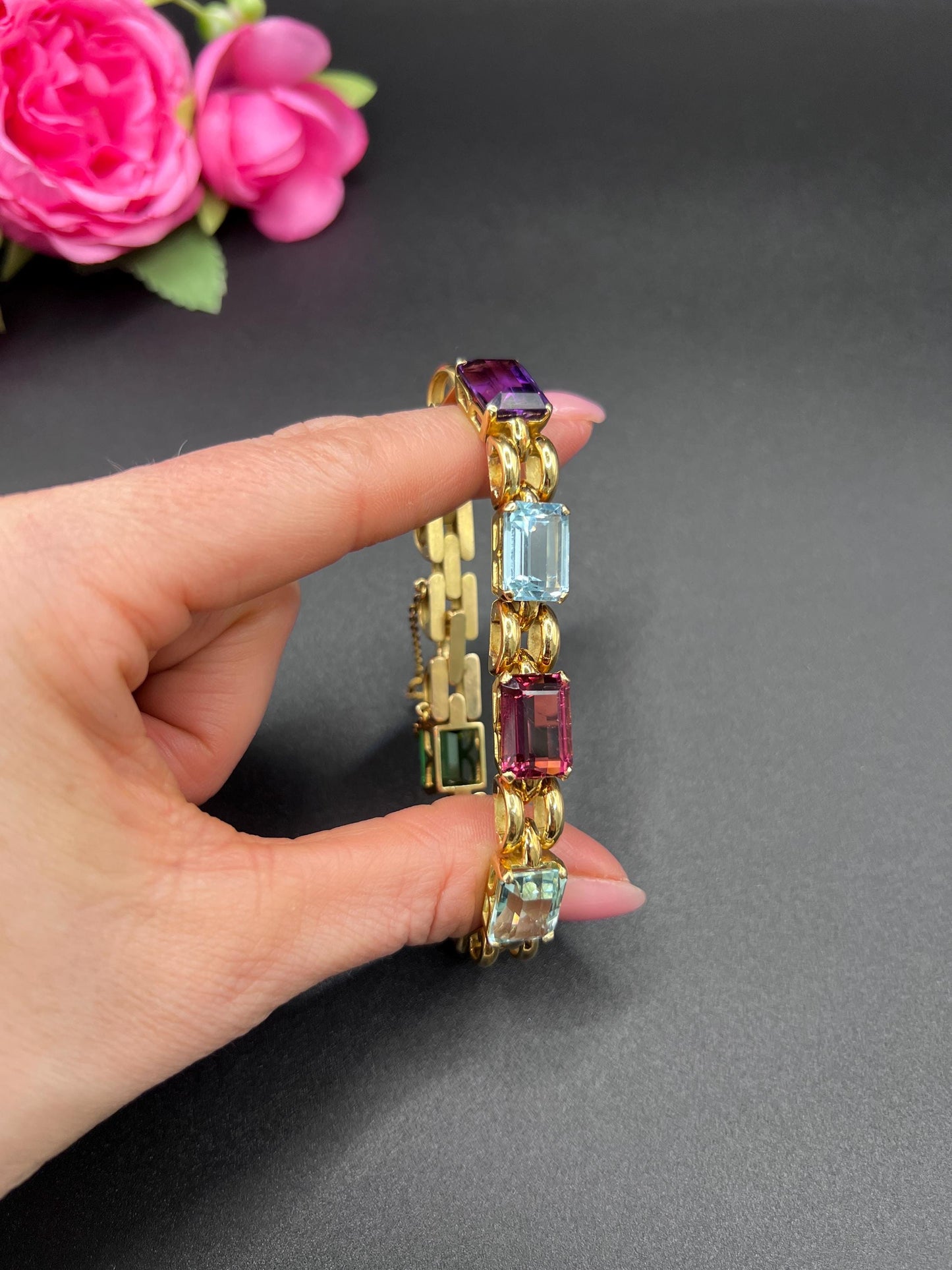 An emerald cut multi-gemstone bracelet in yellow gold, held in a hand
