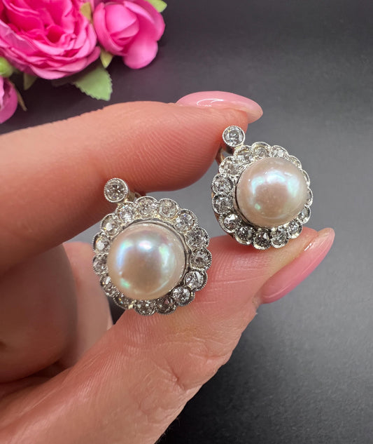 A pair of pearl and old cut diamond floral cluster earrings, held in a hand