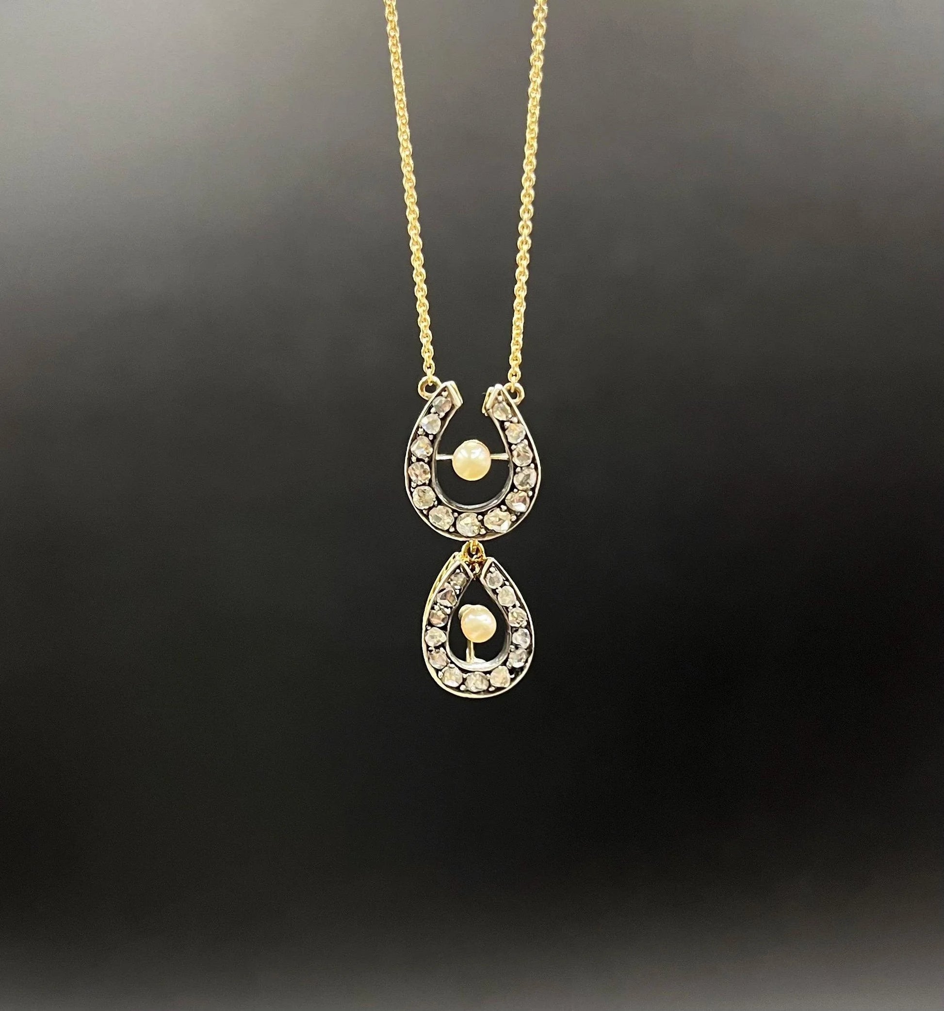 A pearl and diamond set doube horseshoe pendant on a gold chain