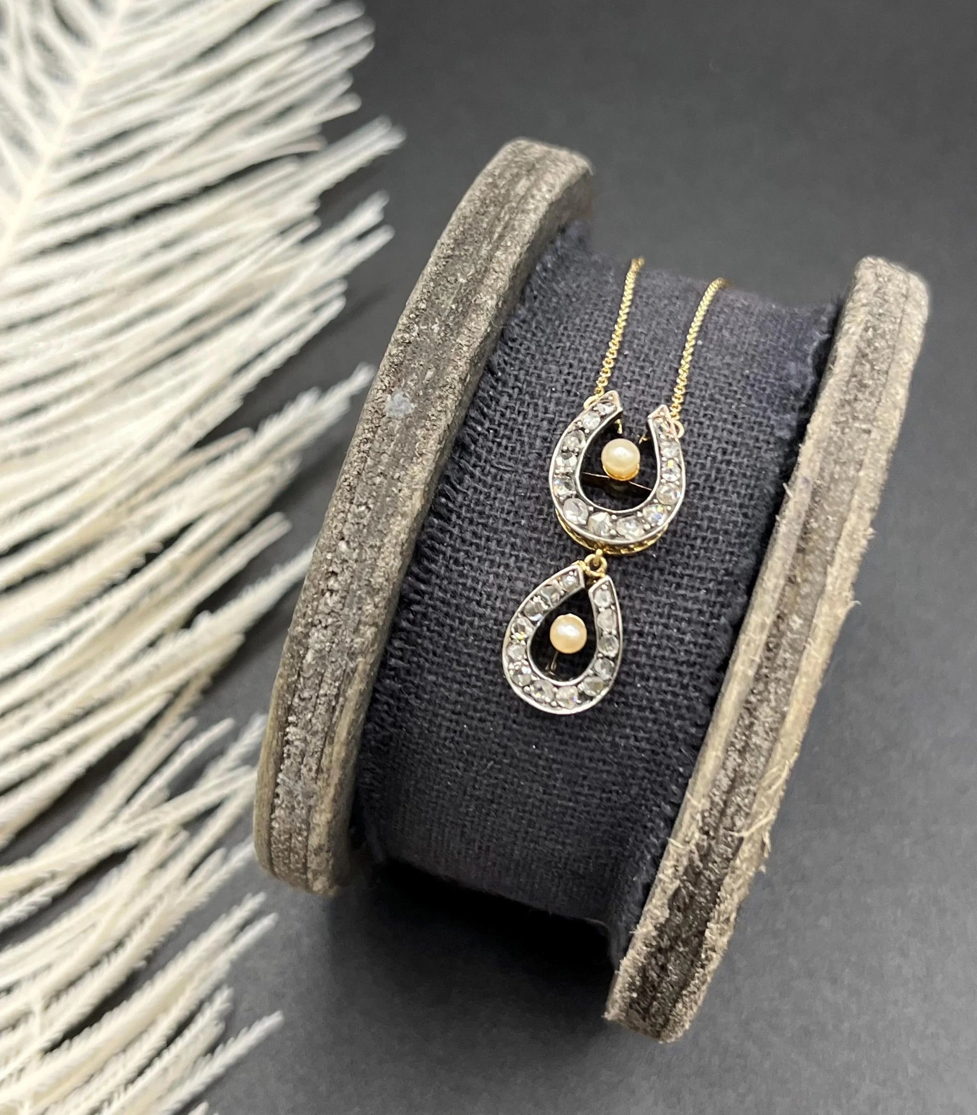 A pearl and diamond set doube horseshoe pendant on a gold chain