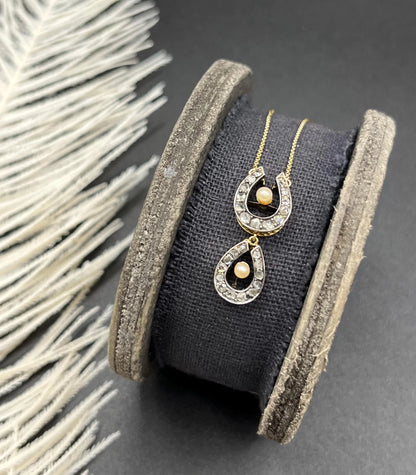 A pearl and diamond set doube horseshoe pendant on a gold chain