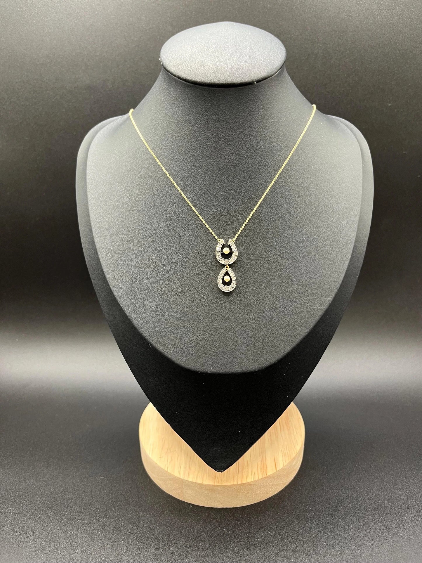 A pearl and diamond set doube horseshoe pendant on a gold chain