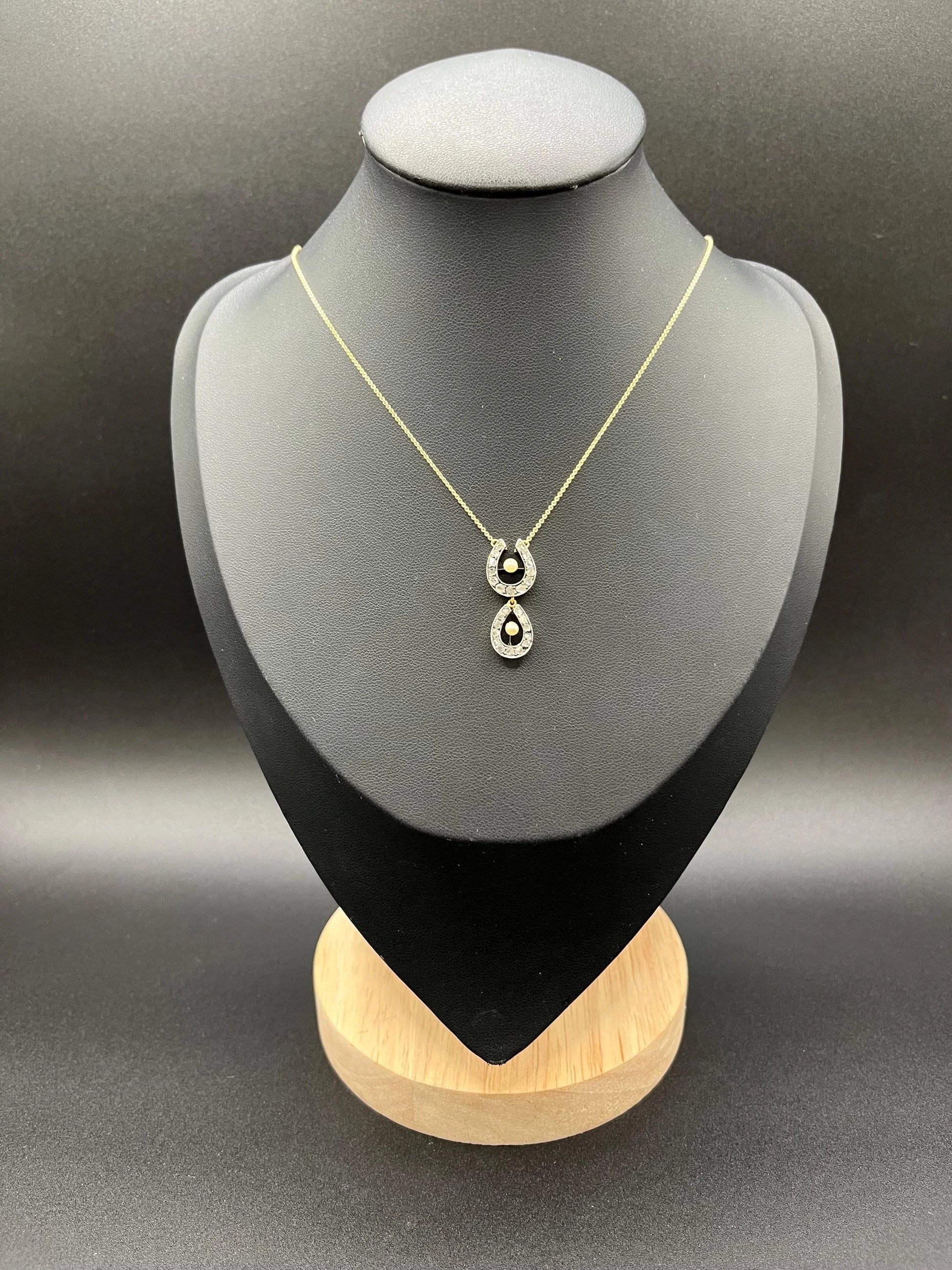 A pearl and diamond set doube horseshoe pendant on a gold chain