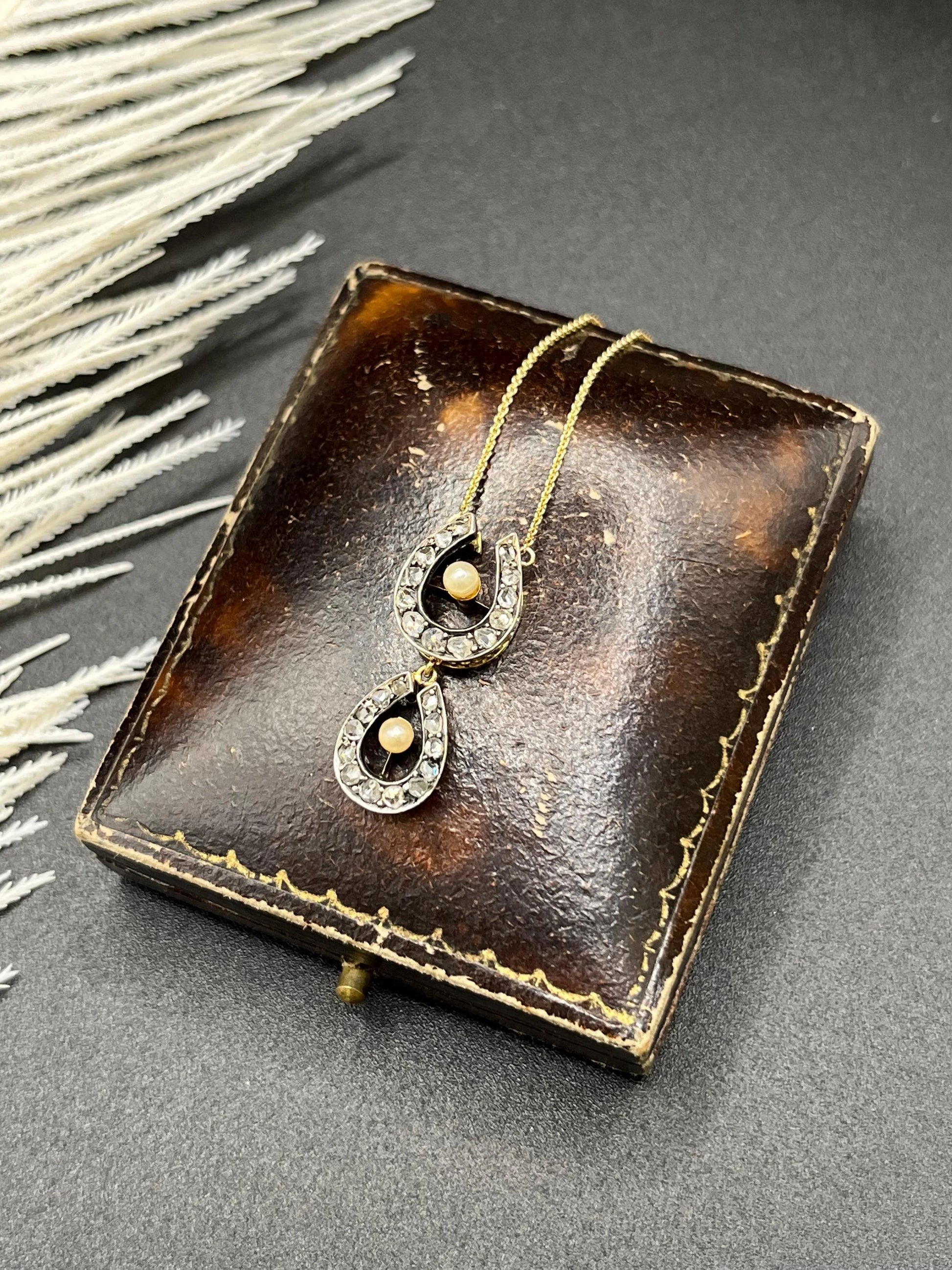 A pearl and diamond set doube horseshoe pendant on a gold chain