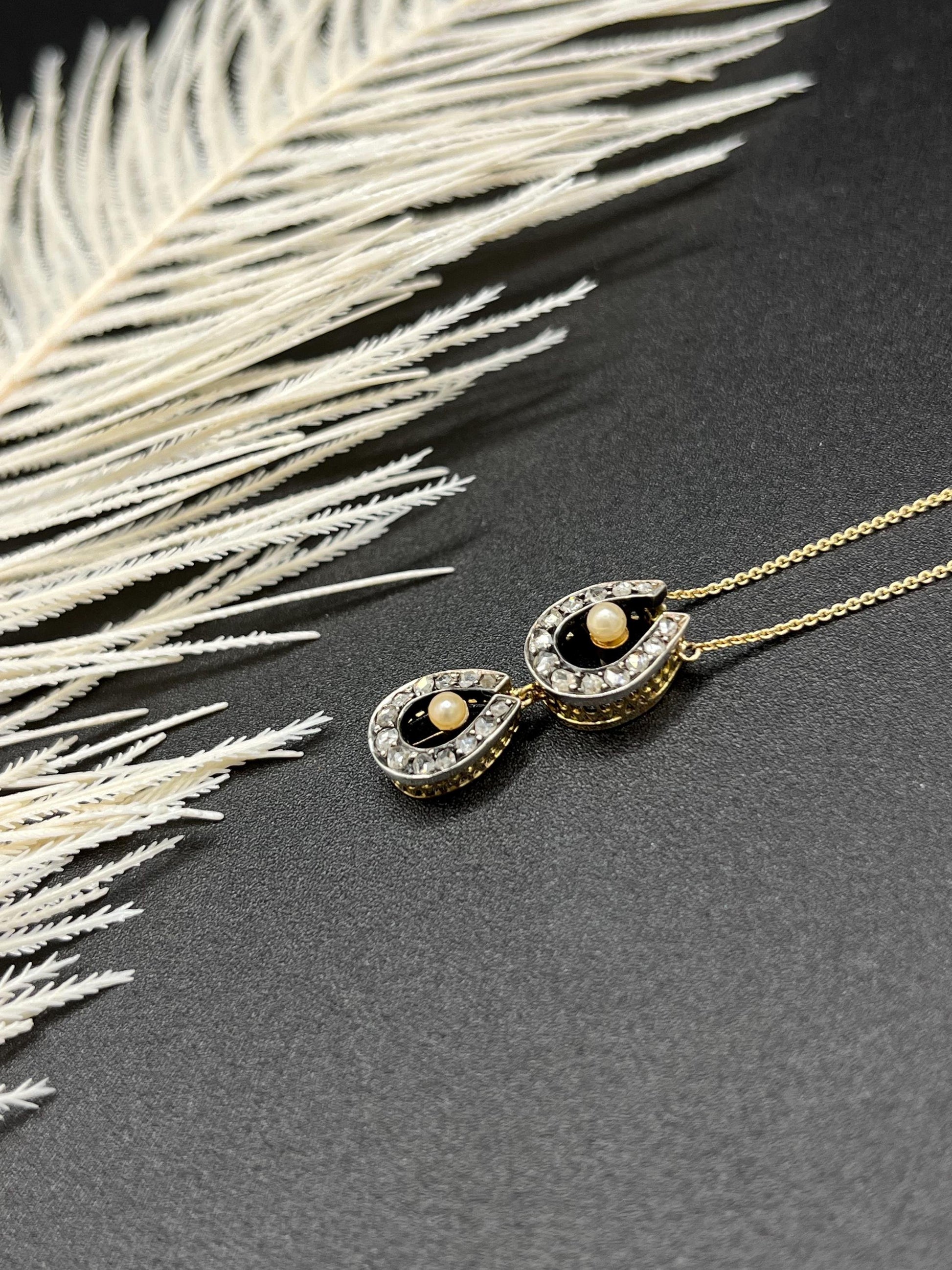 A pearl and diamond set doube horseshoe pendant on a gold chain
