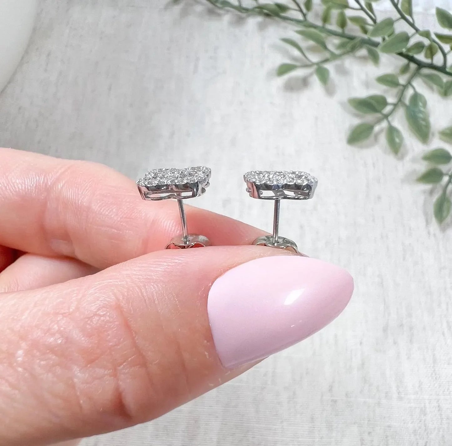 A pair of white gold clover shaped diamond cluster stud earrings, held in a hand
