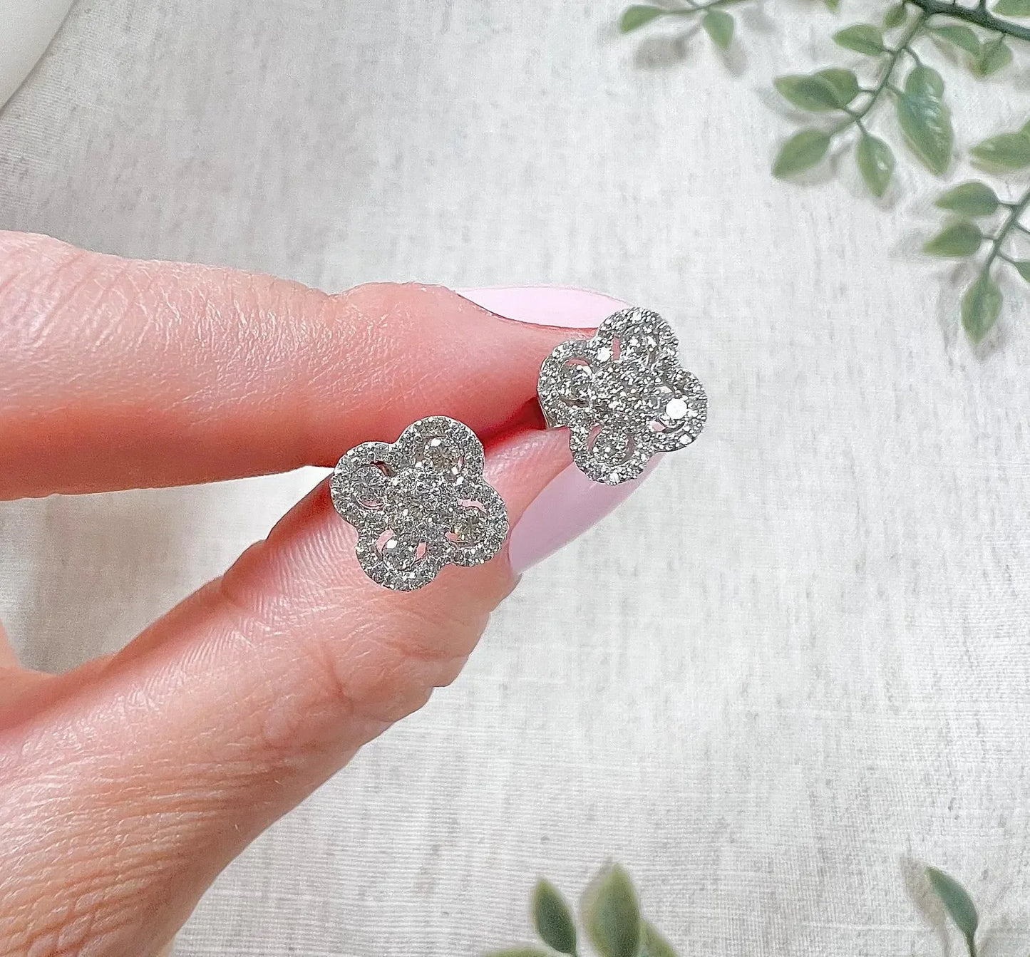 A pair of white gold clover shaped diamond cluster stud earrings, held in a hand