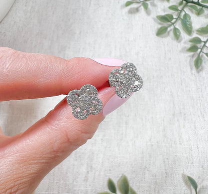 A pair of white gold clover shaped diamond cluster stud earrings, held in a hand