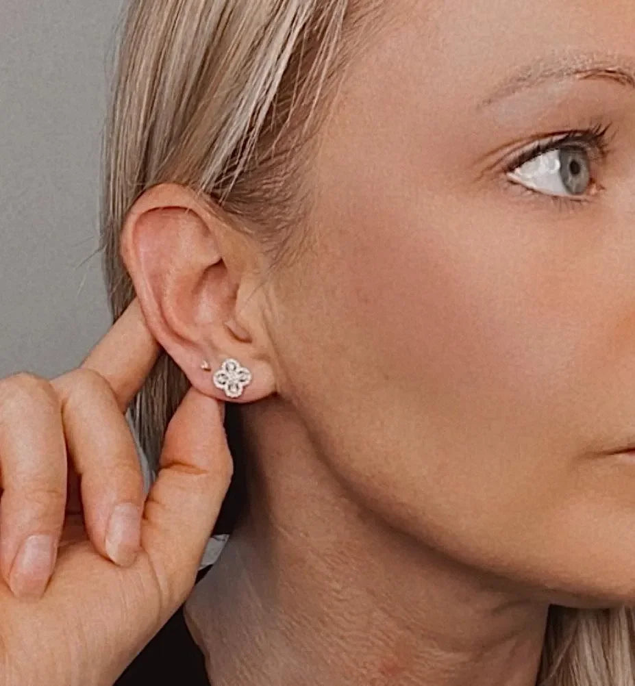 A white gold clover shaped diamond cluster stud earring, modelled in an ear