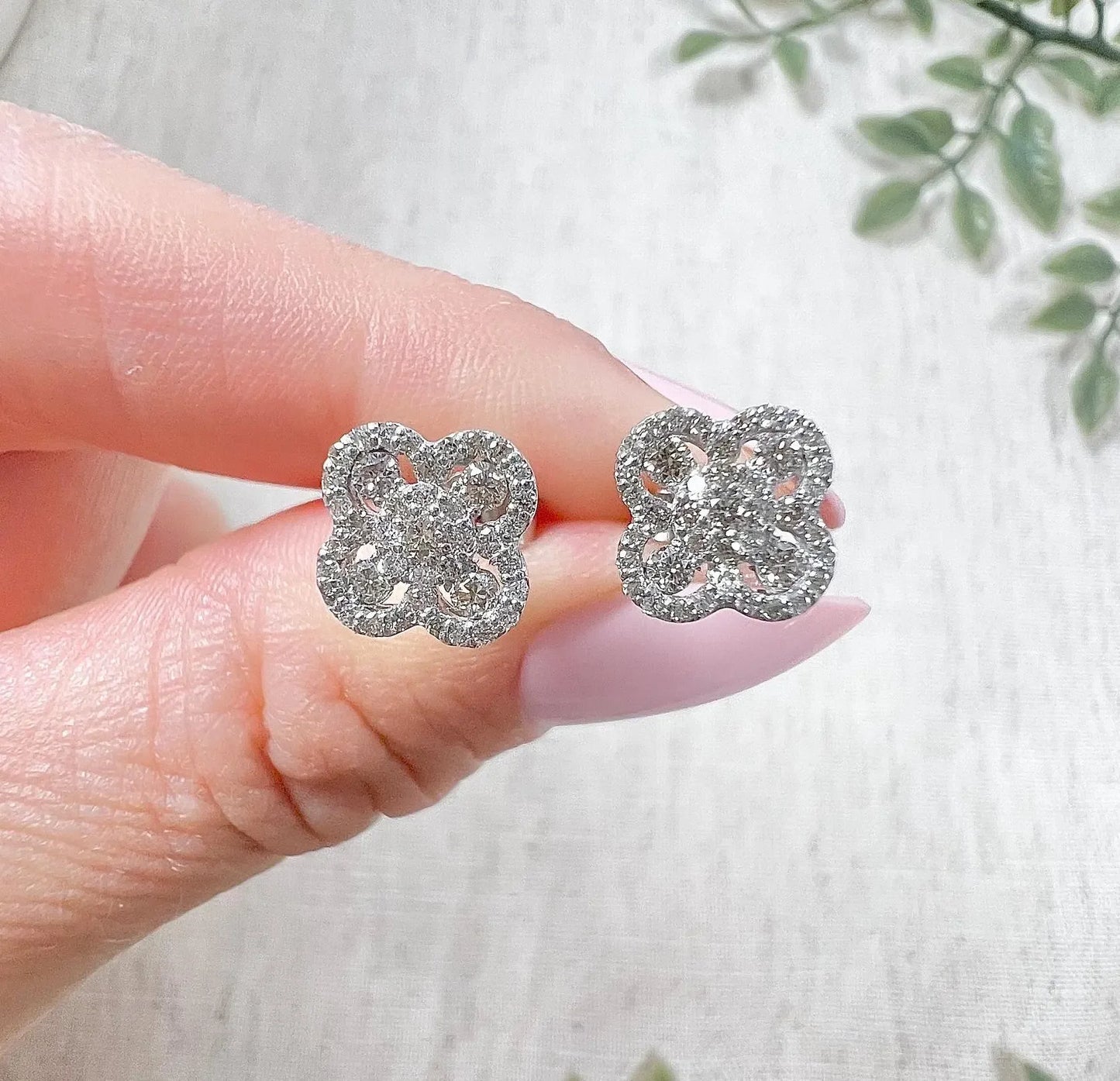 A pair of white gold clover shaped diamond cluster stud earrings, held in a hand