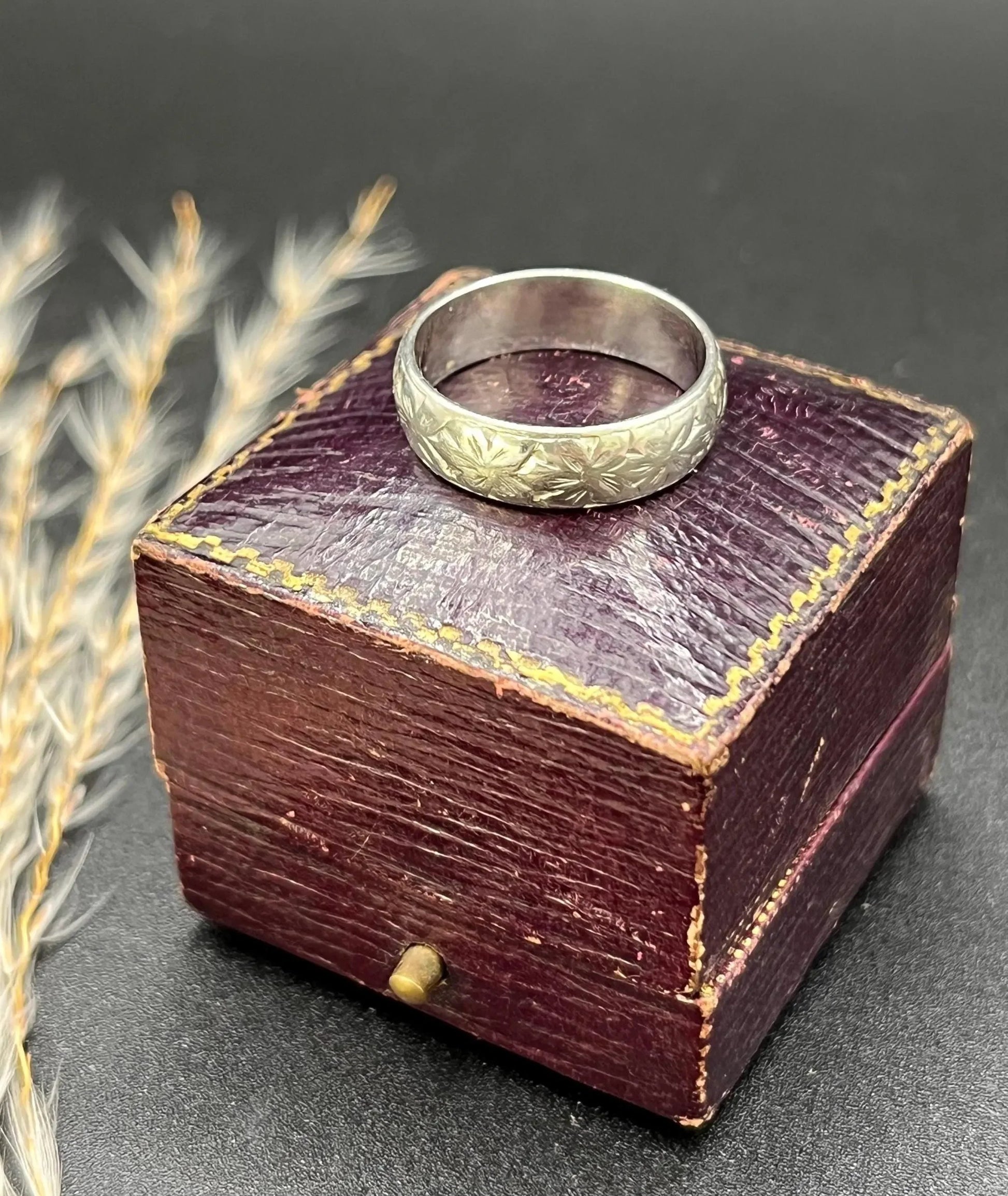An engraved platinum wedding band ring, on an antique ring box