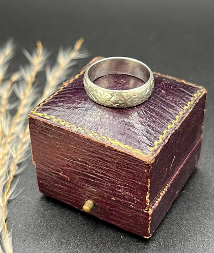 An engraved platinum wedding band ring, on an antique ring box