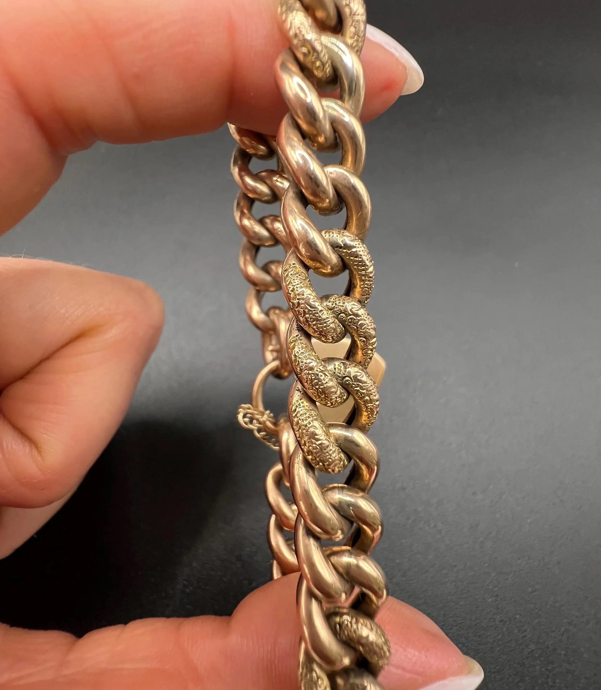A rose gold curb link bracelet with engraved heart padlock clasp, held in a hand