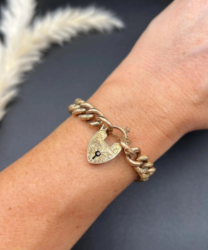 A rose gold curb link bracelet with engraved heart padlock clasp, modelled on a wrist