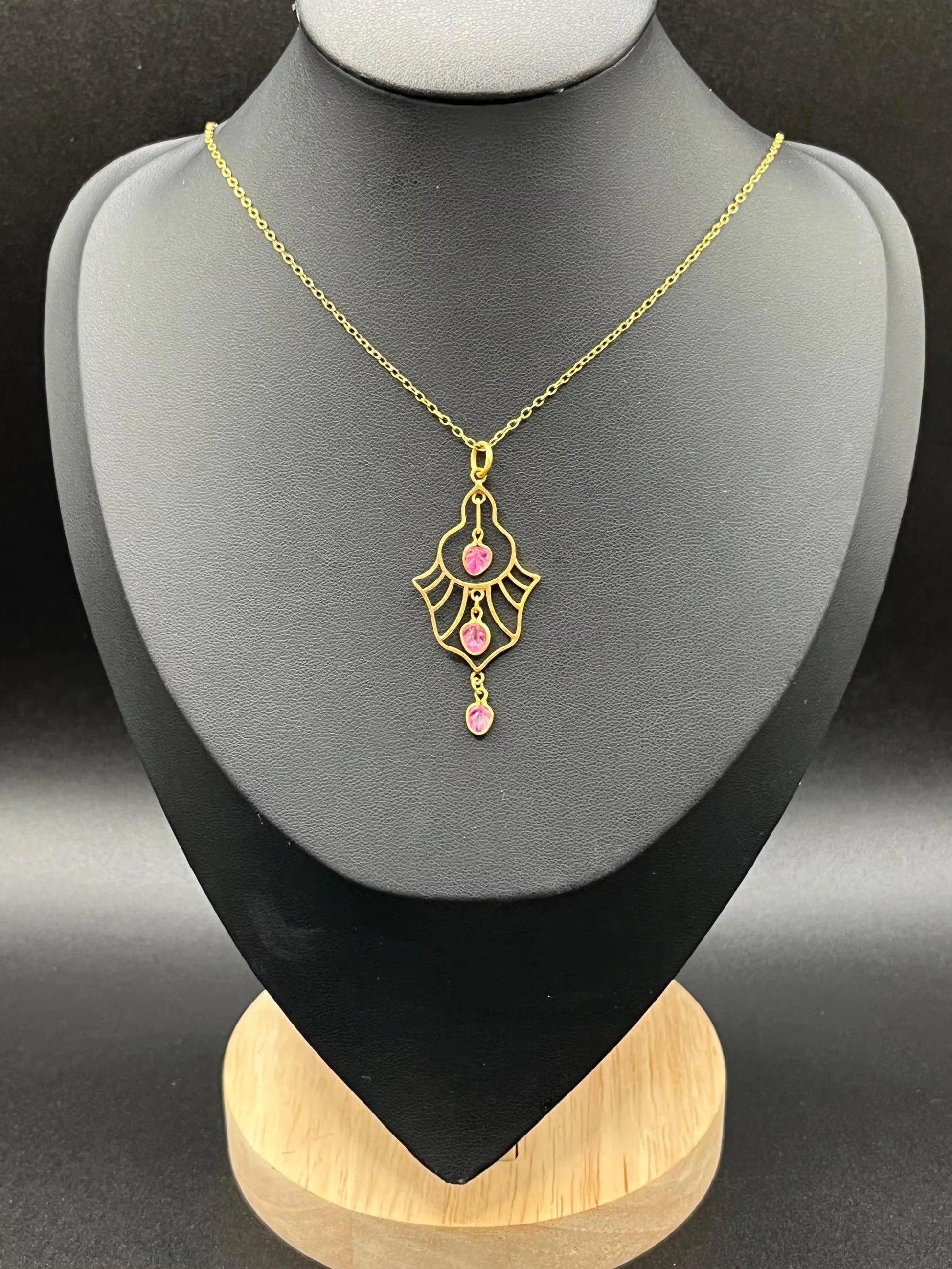 A yellow gold three stone ruby openwork drop pendant on a yellow gold chain, on a black jewellery bust