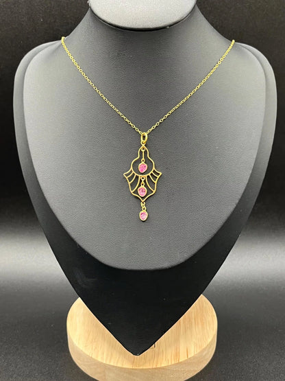A yellow gold three stone ruby openwork drop pendant on a yellow gold chain, on a black jewellery bust