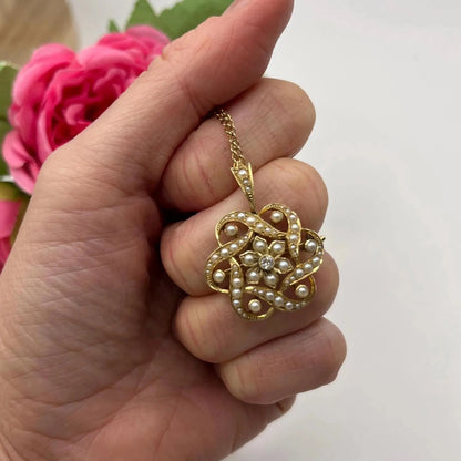 A yellow gold seed pearl and diamond floral brooch/pendant, with a chain, held in a hand