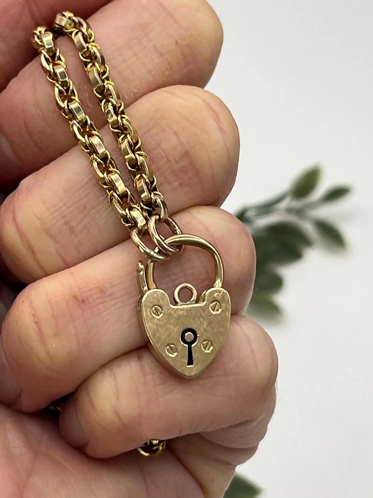 A yellow gold chain necklace with a heart shaped padlock clasp, held in a hand